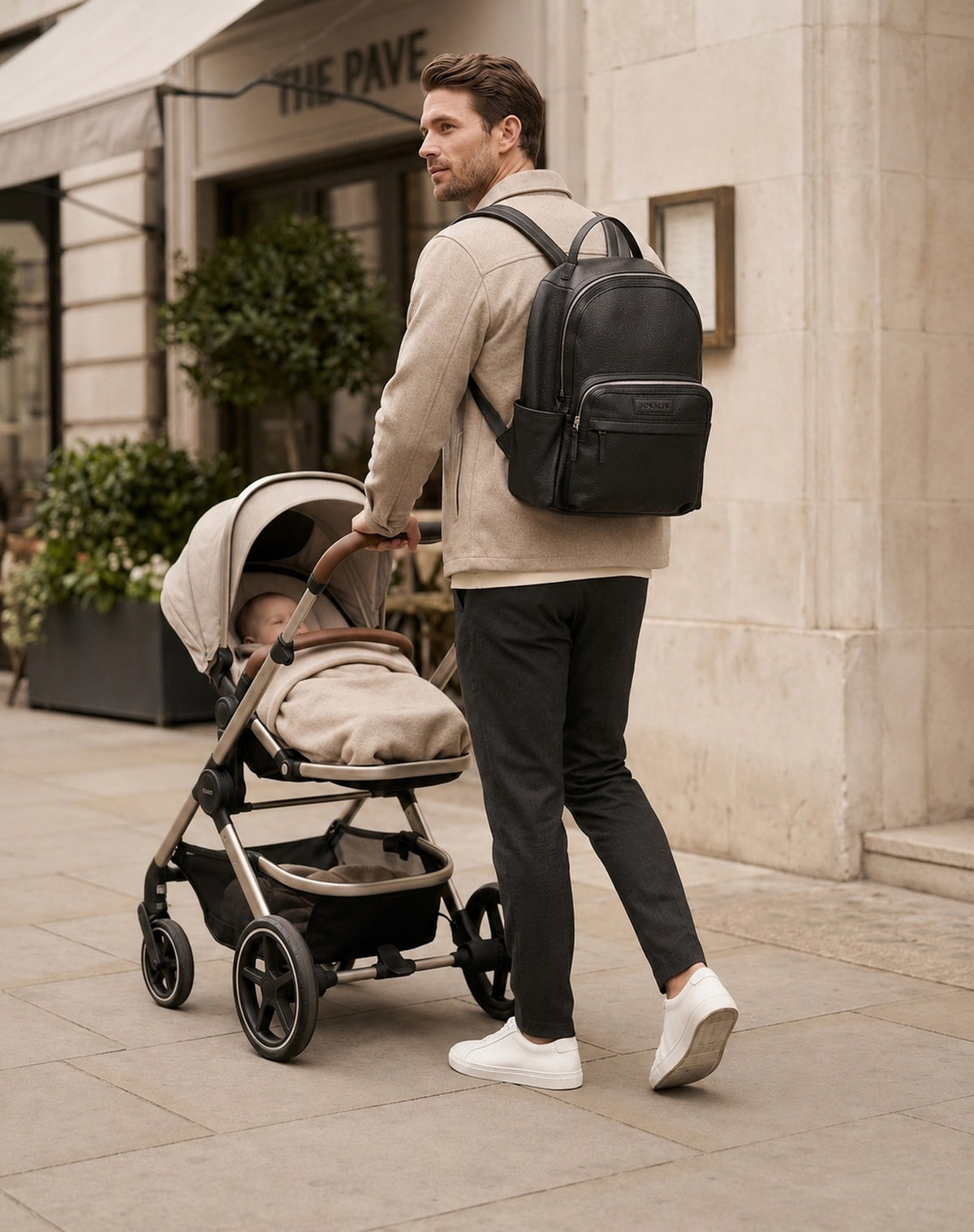 The Aurelia nappy bag being carried by a father while pushing a pram with a sleeping baby on a city street 