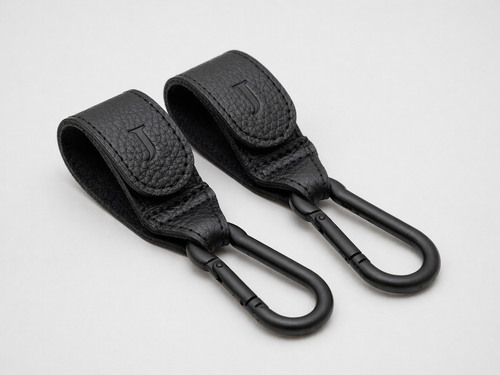 Two black leather Buggy clips with matte black carabiners and an embossed J logo on the front, sitting on a white background 